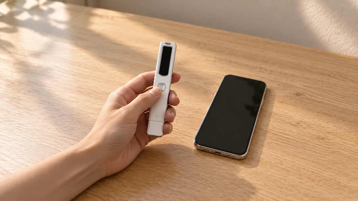 A hand holding a slim white PR200 Bluetooth call recorder next to an iPhone lying face up on a light oak desk.